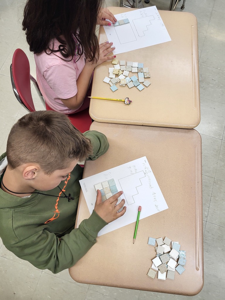 Students in a 3rd grade classroom working on math activities involving area and perimeter, using shapes and hands-on materials.