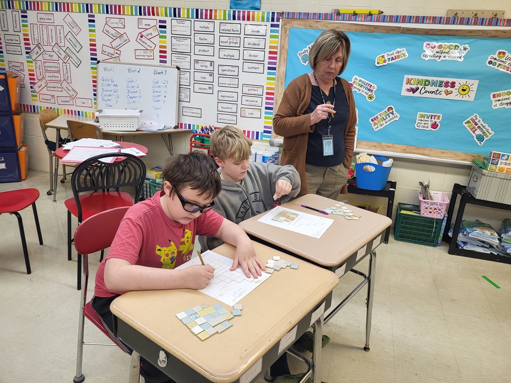 Students in a 3rd grade classroom working on math activities involving area and perimeter, using shapes and hands-on materials.