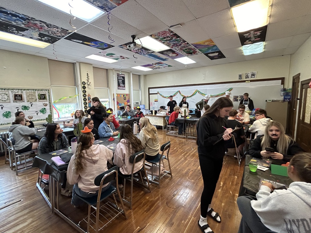Spanish II students serving authentic Hispanic food to classmates and staff during a classroom restaurant project with menus and dine-in dining tables.