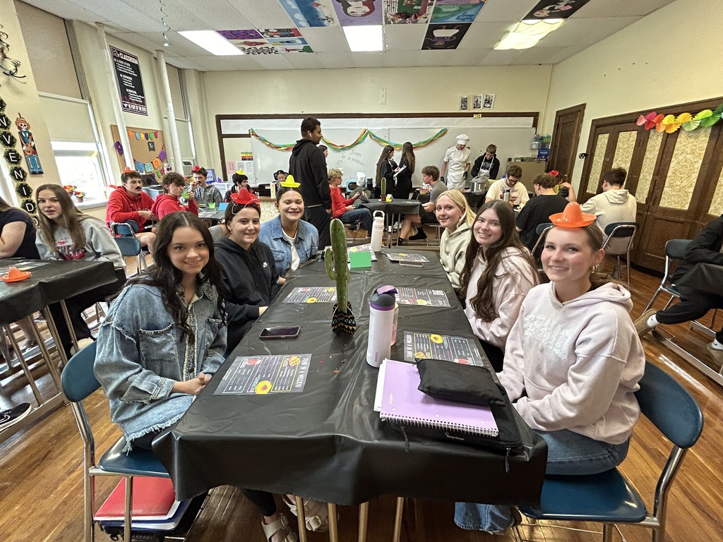 Spanish II students serving authentic Hispanic food to classmates and staff during a classroom restaurant project with menus and dine-in dining tables.