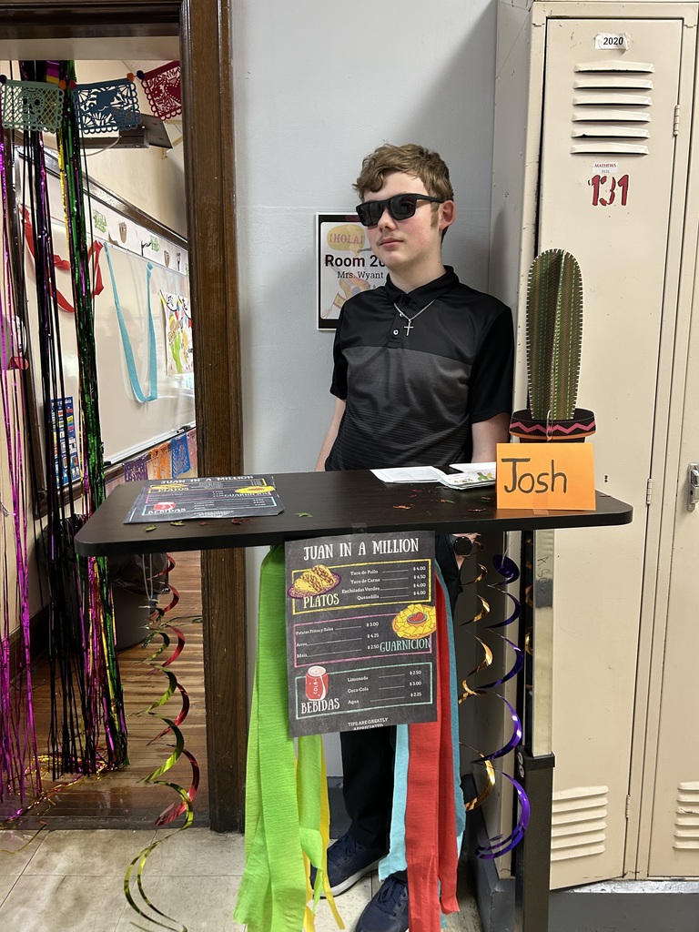 Spanish II students serving authentic Hispanic food to classmates and staff during a classroom restaurant project with menus and dine-in dining tables.