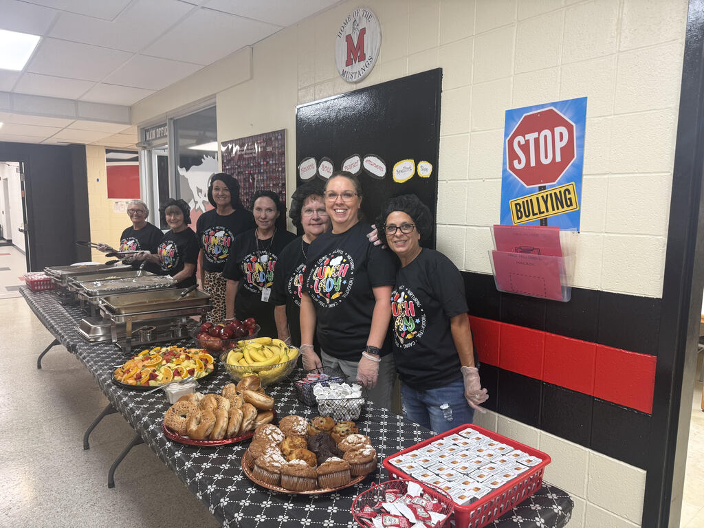 Food service staff members gathered around a table filled with breakfast foods they prepared for staff on the first day of school.
