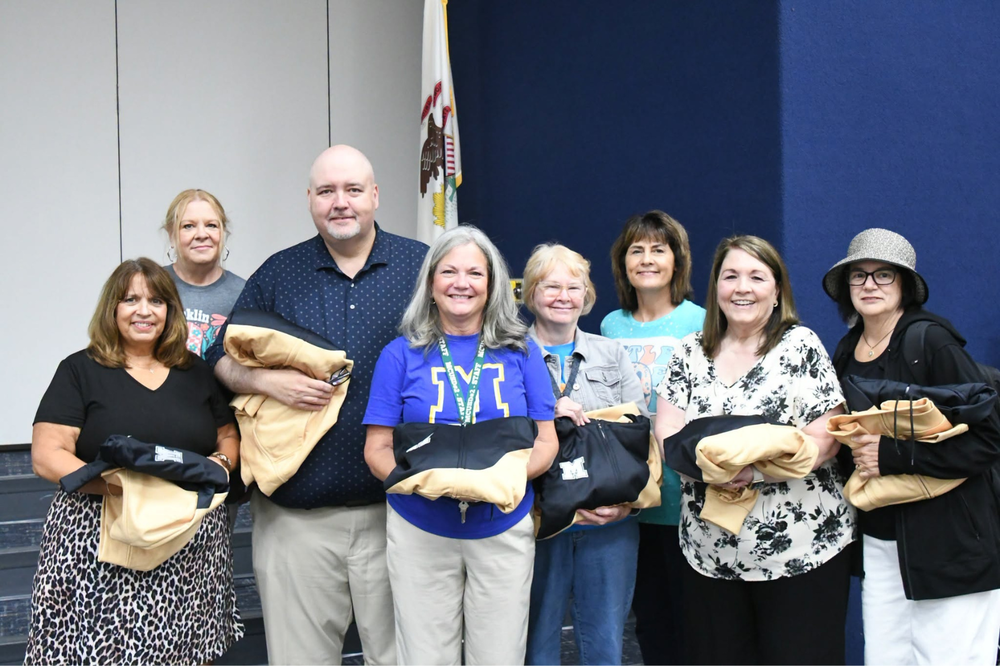 Group photo of 2027 retirees at the back to school breakfast. Holding sweatshirts