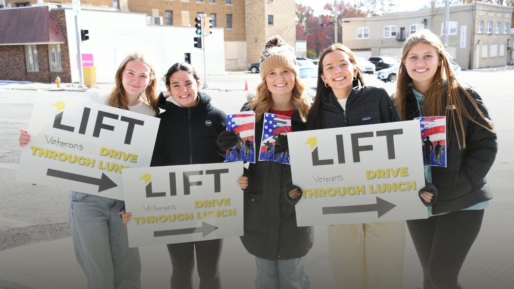 LIFT students holding signs outside promoting the LIFT Veterans Drive Through Lunch. Five female students are pictured.
