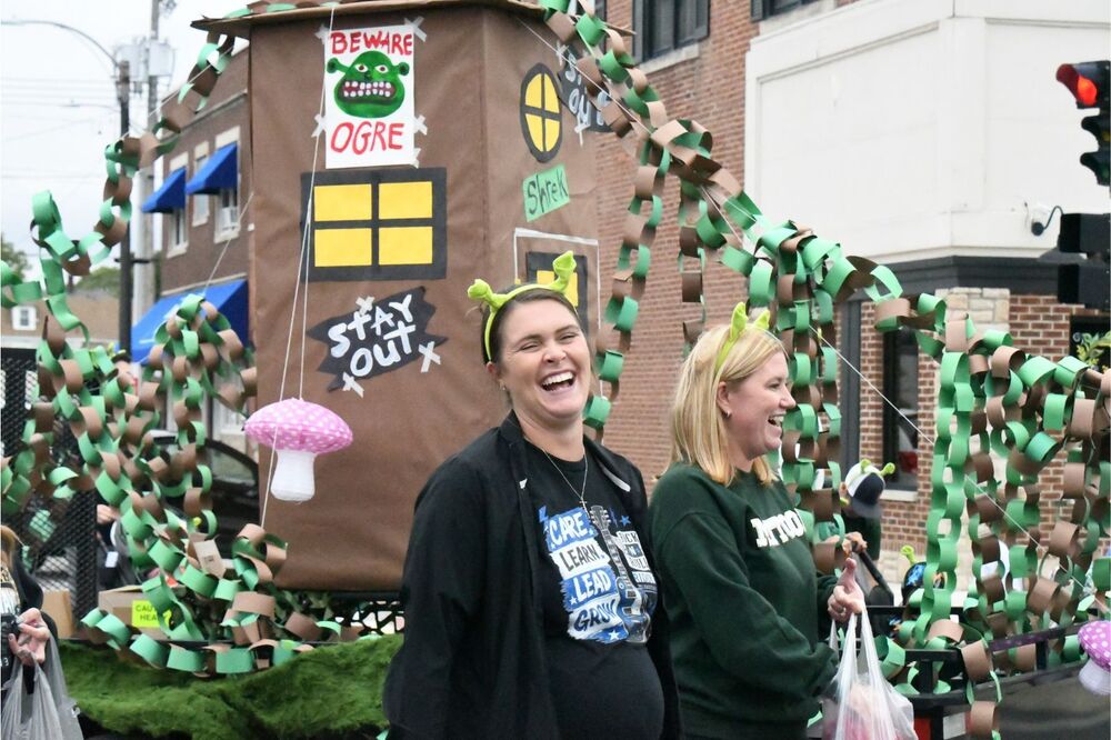 two riddle staff members laughing and passing out candy next to their shrek float at hoco parade