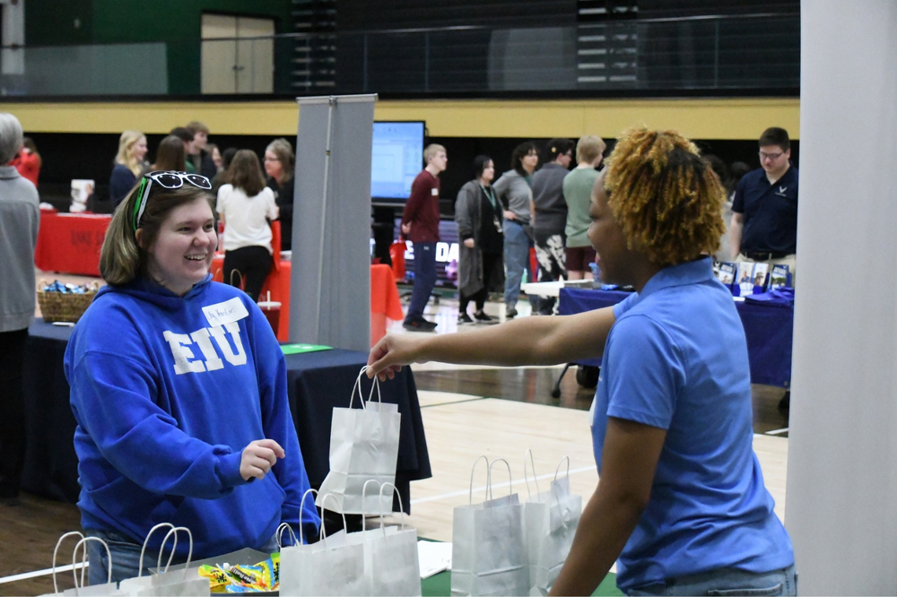 Futures Day event. Student is accepting a bag from a college representative in the gym