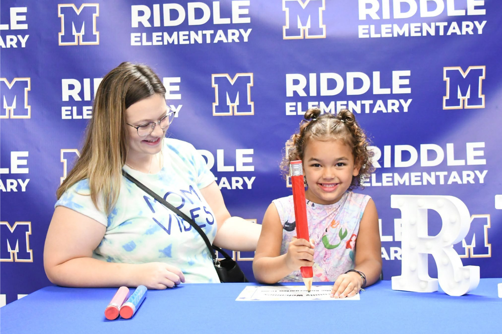 Kindergartener signing on with her guardian watching at signing day