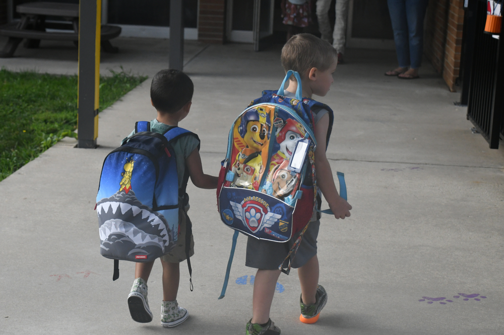 Two Franklin students holding hands walking into school with their backpacks on their back