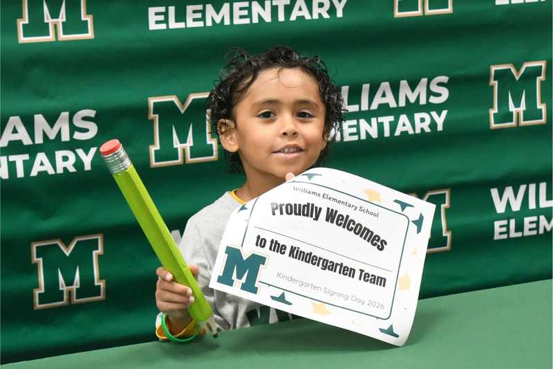 Kindergartener holding up certificate and pencil at signing days