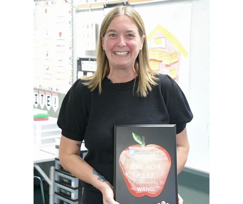 Brenda Bell holding up her WAND Educator of the Month plaque in her classroom at Williams Elementary School