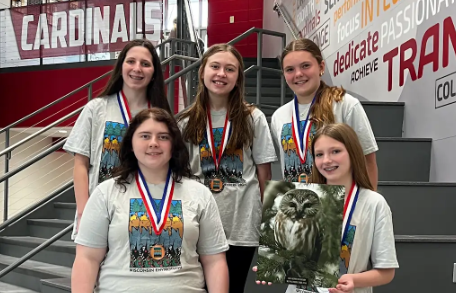 Students smiling with medals around their necks holding artwork and standing on the Cardinal Lobby stairs in MHS