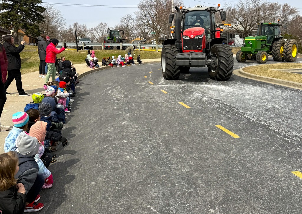 FFA students and staff drove their tractors to school on Tuesday in honor of National Ag Day. Early learning students bundled up and sitting on curb in front of  Parkview Early Learning Center waving to high school FFA students driving by in red and green tractors. 