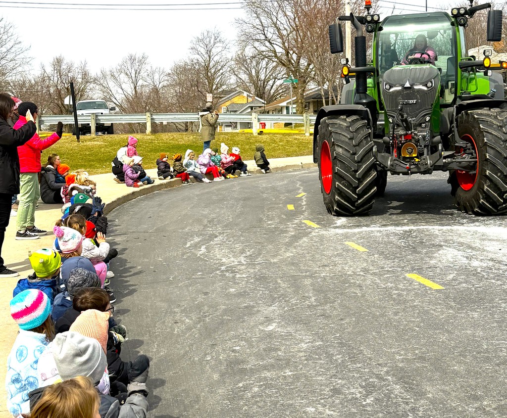 FFA students and staff drove their tractors to school on Tuesday in honor of National Ag Day. Early learning students bundled up and sitting on curb in front of  Parkview Early Learning Center waving to high school FFA students driving by in red and green tractors. 