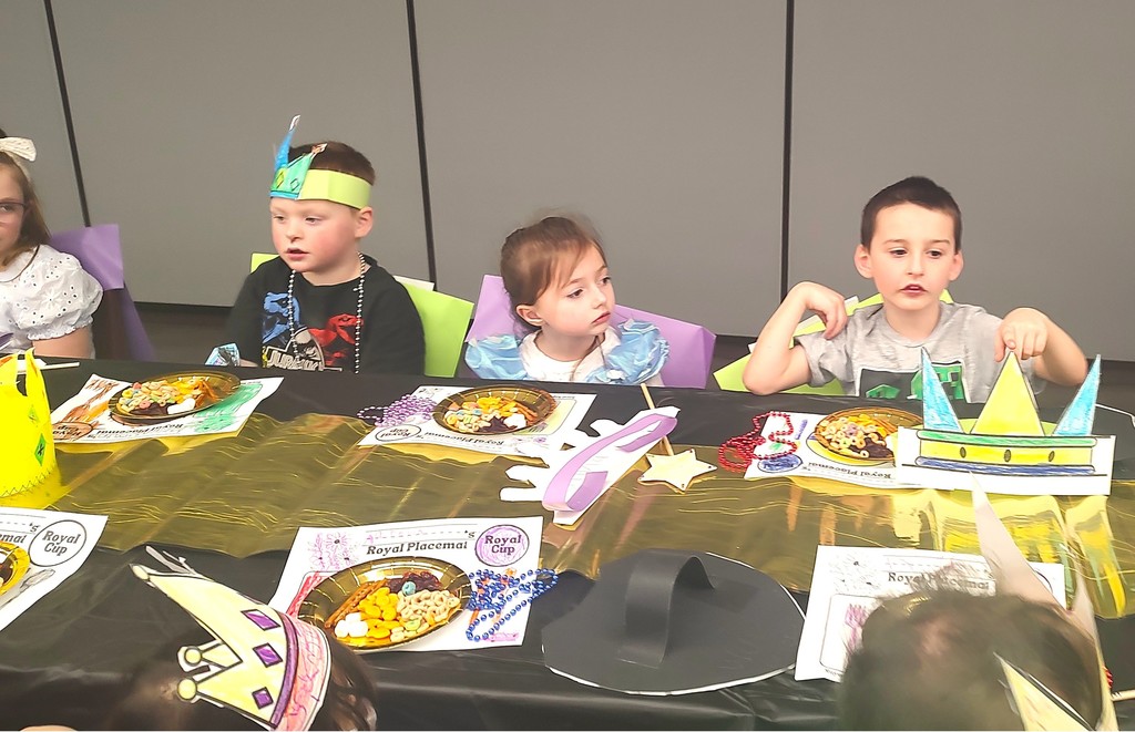 5K students dressed with king and queen crowns and seated at a long table in the auditorium with placemats