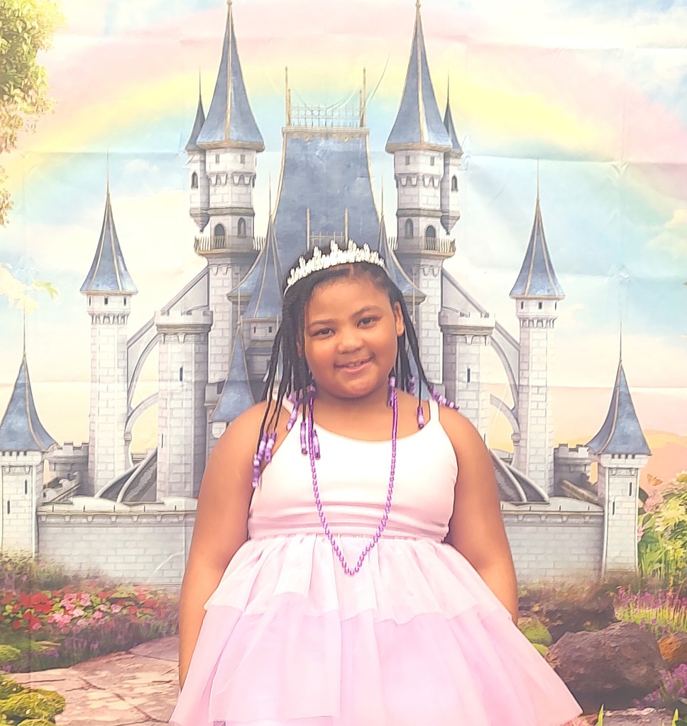 child dressed in royal crown smiling in front of backdrop with castle