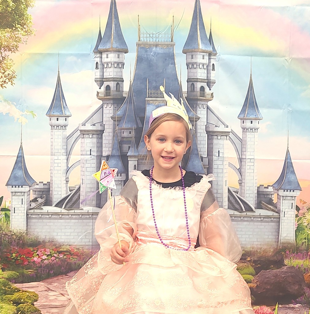 child dressed in royal crown smiling in front of backdrop with castle