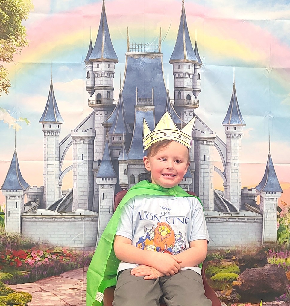 child dressed in royal crown smiling in front of backdrop with castle