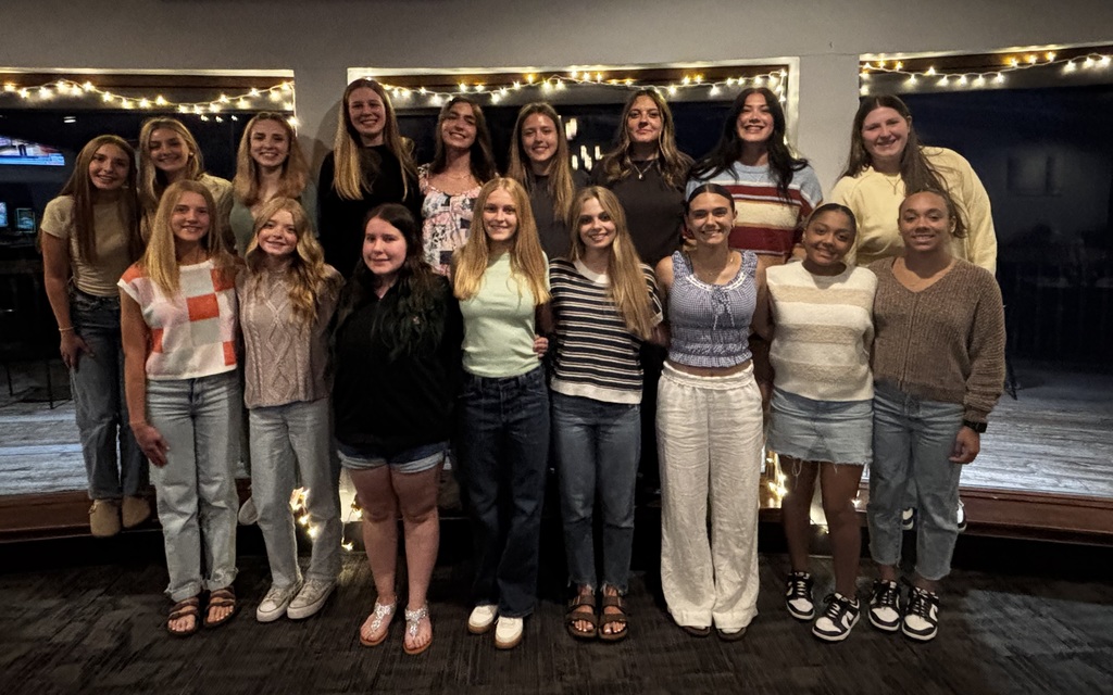 Group photo of basketball girls with picture windows and white string lights in background