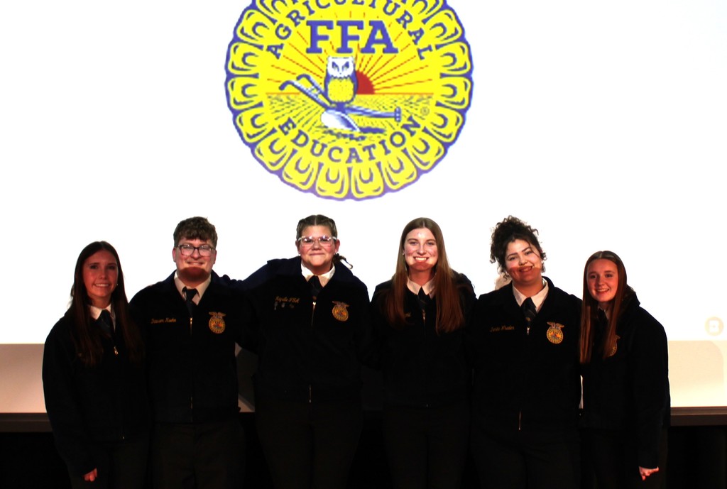 FFA students smiling for photo on auditorium stage with FFA emblem in the background