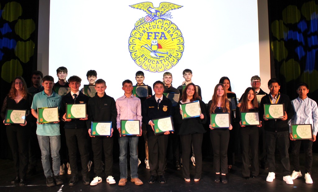 FFA students smiling for photo on auditorium stage with degree certificates and FFA emblem in the background