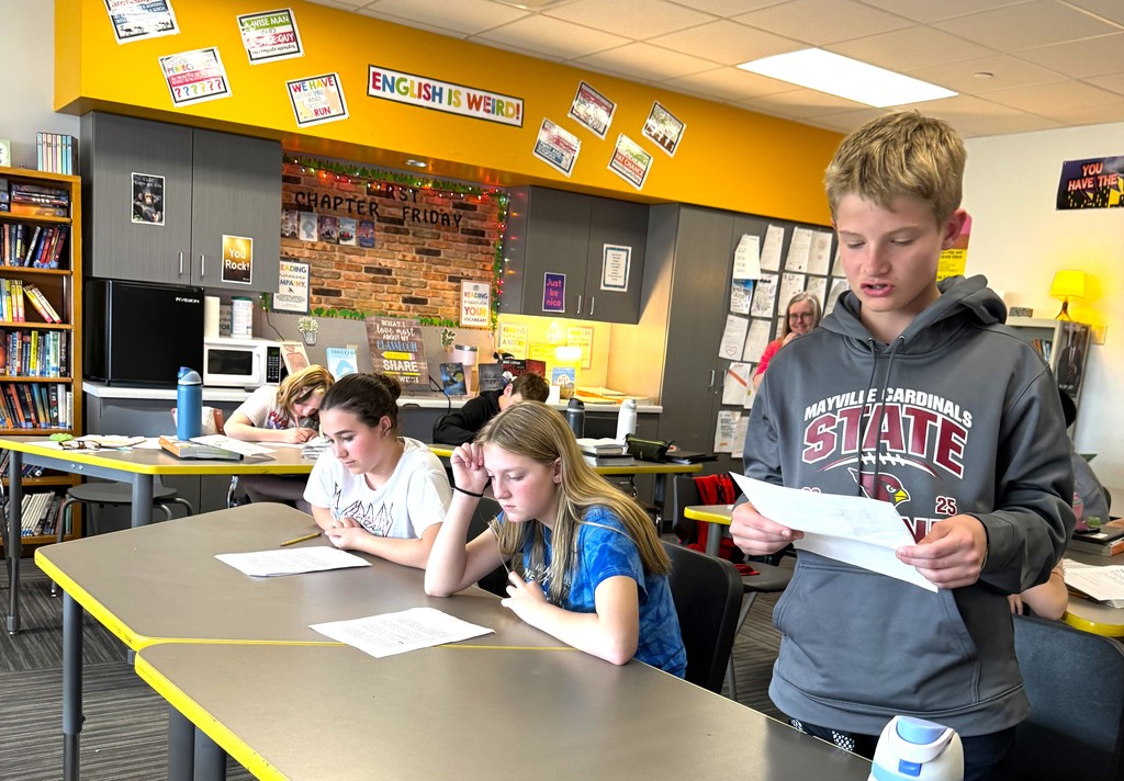 7th graders in Mrs. Perkins' classroom participating in a mock trial as part of their ELA class, reading arguments they've prepared. Mrs. Perkins is dressed in a judge robe with a wooden gavel. 