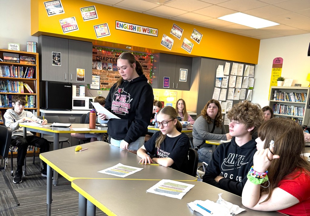 7th graders in Mrs. Perkins' classroom participating in a mock trial as part of their ELA class, reading arguments they've prepared. Mrs. Perkins is dressed in a judge robe with a wooden gavel. 