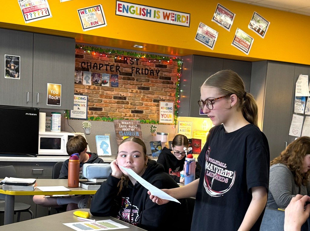 7th graders in Mrs. Perkins' classroom participating in a mock trial as part of their ELA class, reading arguments they've prepared. Mrs. Perkins is dressed in a judge robe with a wooden gavel. 