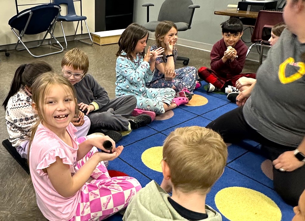 Children smiling and holding baby chicks, sitting on floor in classroom
