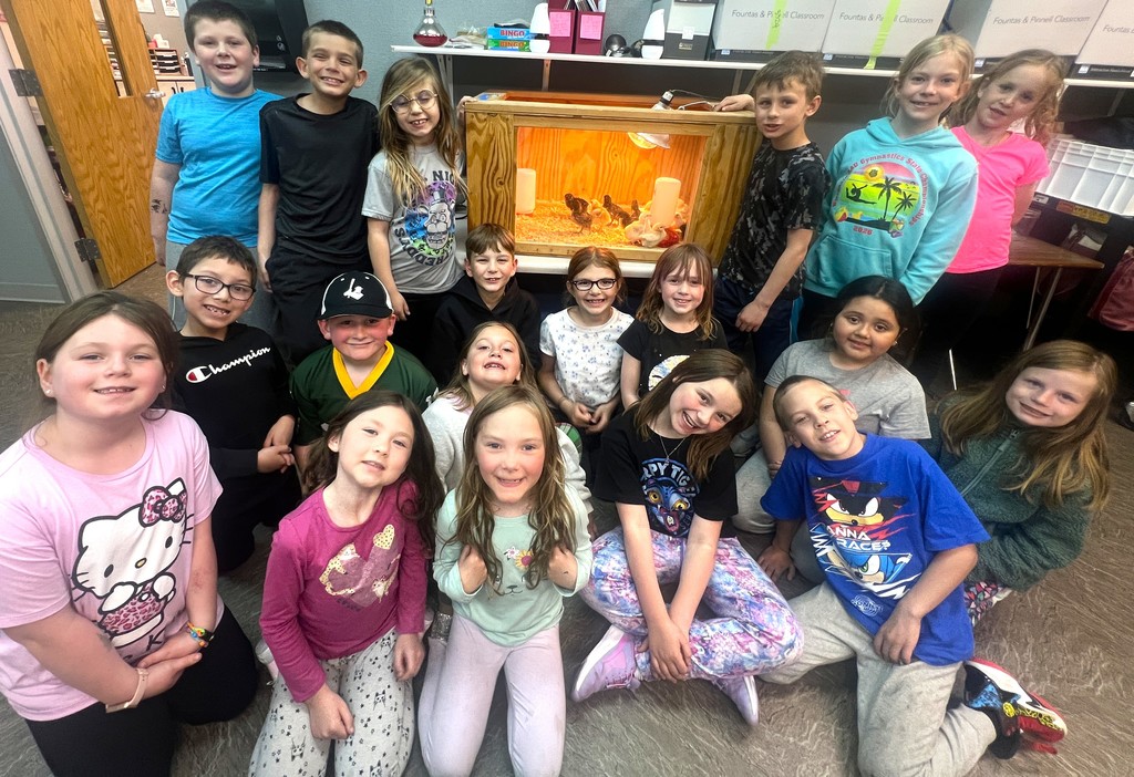 Children smiling and holding baby chicks, sitting on floor in classroom