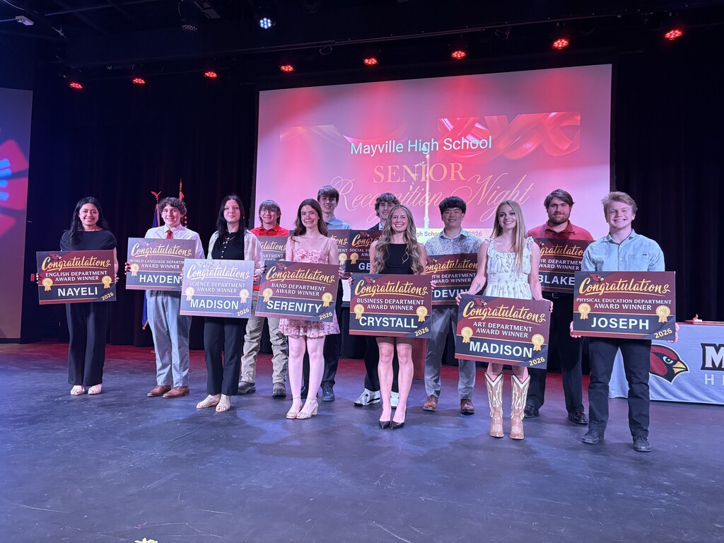 Students smiling and holding department award winner signs on auditorium stage at MHS with MHS Senior Recognition Night graphic displayed on screen behind them