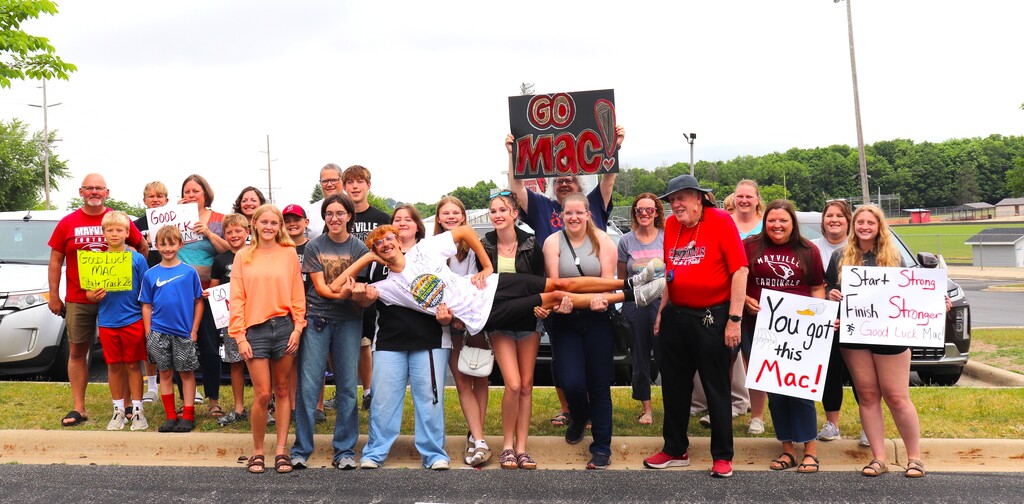 Group of students, staff and friends smiling for State track send-off with signs and posters in school parking lot