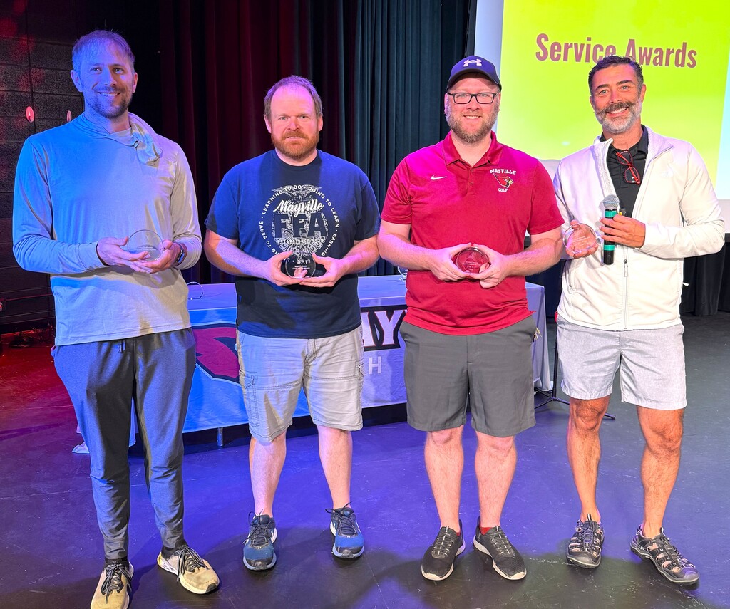 Four staff members smiling on stage at MHS holding crystal awards in celebration of 10 years of service