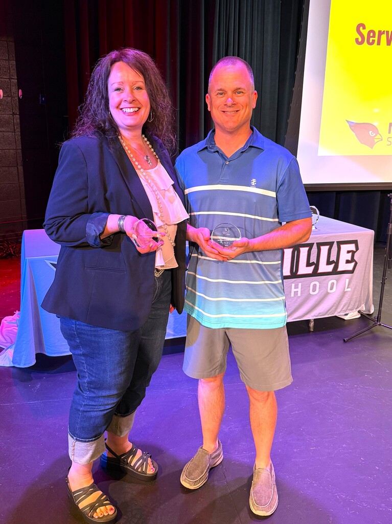 Two staff members on stage at MHS smiling and holding their 30 year service awards