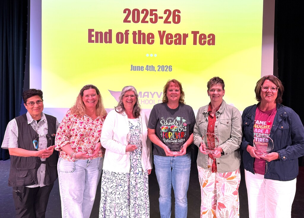 Retirees smiling and holding crystal awards on stage at MHS