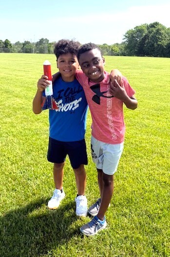 Summer school students out on lawn near school launching rockets and smiling