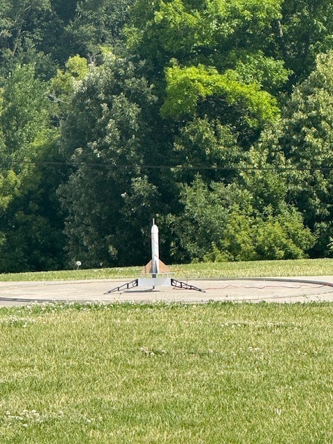 Summer school students out on lawn near school launching rockets and smiling