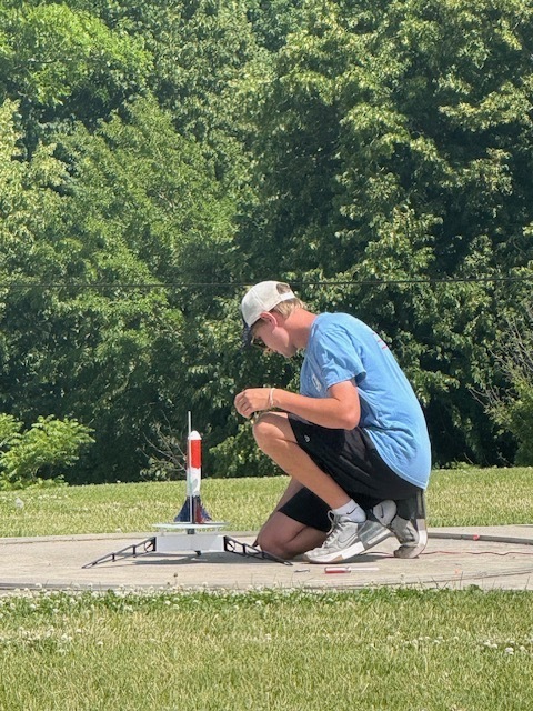 Summer school students out on lawn near school launching rockets and smiling