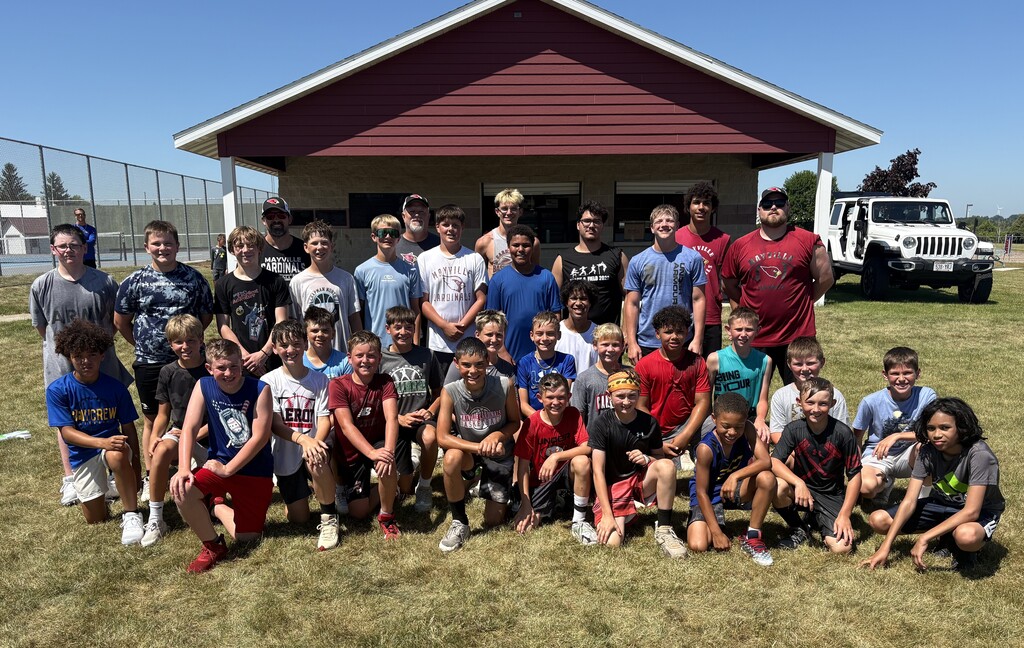 Youth football players with high school volunteers and coaches smiling and posing for group photo after youth summer football camp