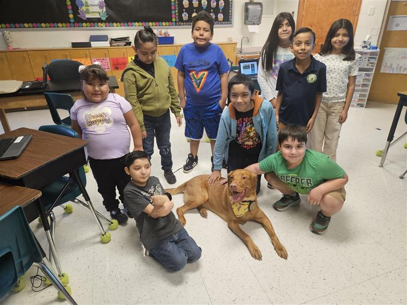 Kids posing with Buddy, the district therapy dog.