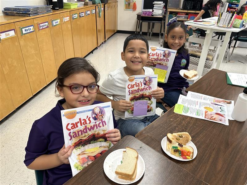 Kids posing with book and sandwich.