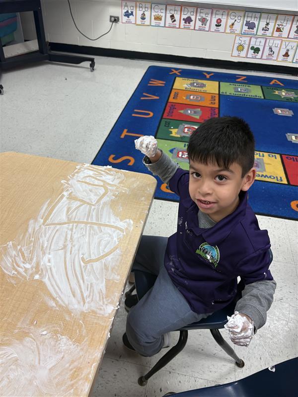 Student working on letters and numbers with shaving cream.