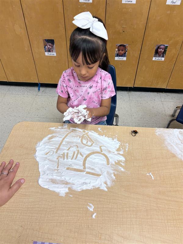 Student working on letters and numbers with shaving cream.