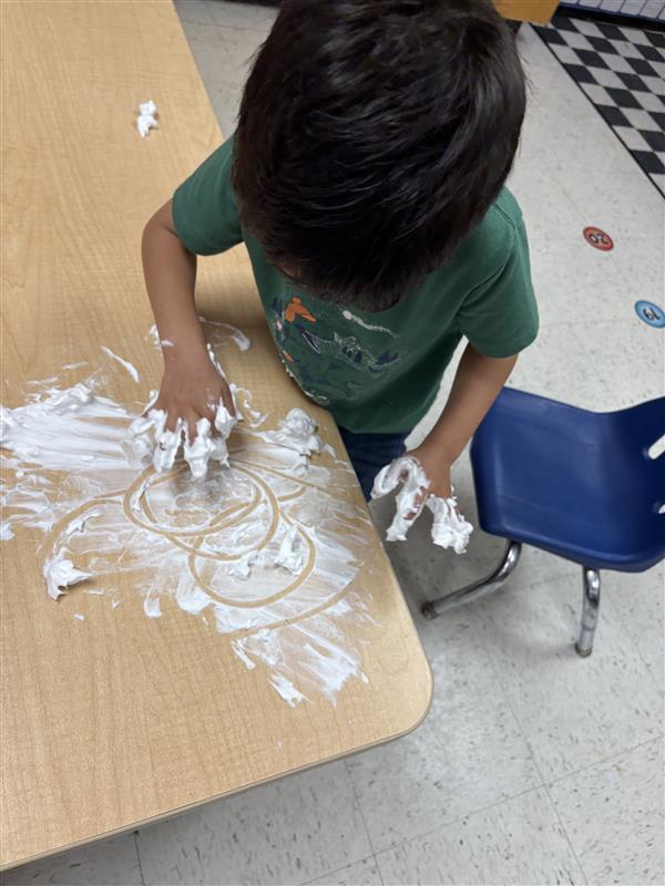Student working on letters and numbers with shaving cream.