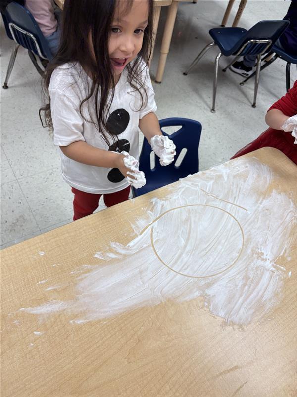 Student working on letters and numbers with shaving cream.
