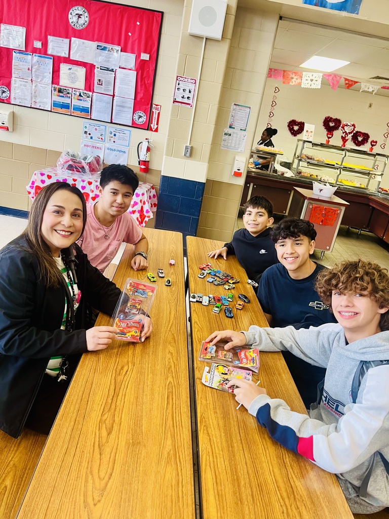 Picture of 8th grade group of boys sitting around a cafeteria table, with many toy cars and principal Trevino