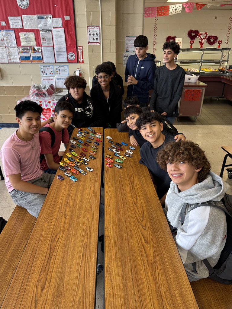 Picture of 8th grade group of boys sitting around a cafeteria table, with many toy cars. 