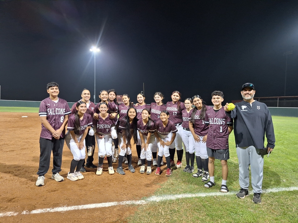 Fossum Middle School Lady Falcons softball team posing together on the field at night after a game, wearing maroon jerseys and white pants with coaches standing beside them.