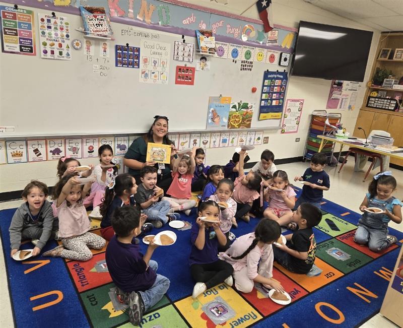 Kids  posing with empanadas while teacher holds book.
