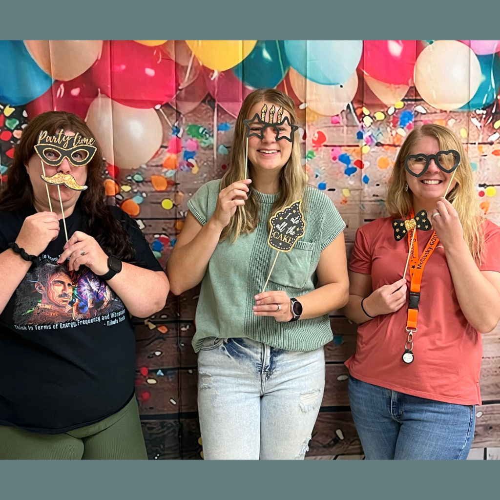 Three ladies posing with birthday props in front of a celebration backdrop