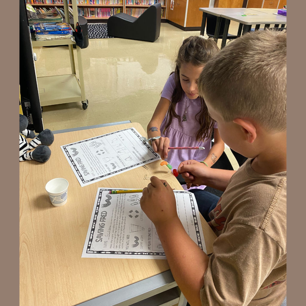 Elementary students observing and taking notes on a gummy worm